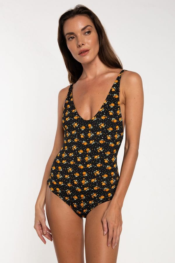 Casino One Piece color Boho Silkana A woman wearing a black one-piece swimsuit with a yellow and orange floral pattern stands against a plain white background.